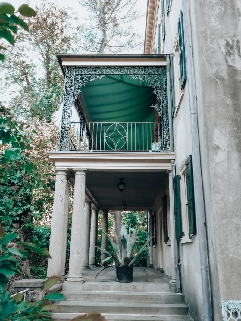 A wrought-iron balcony with a green awning above a columned porch