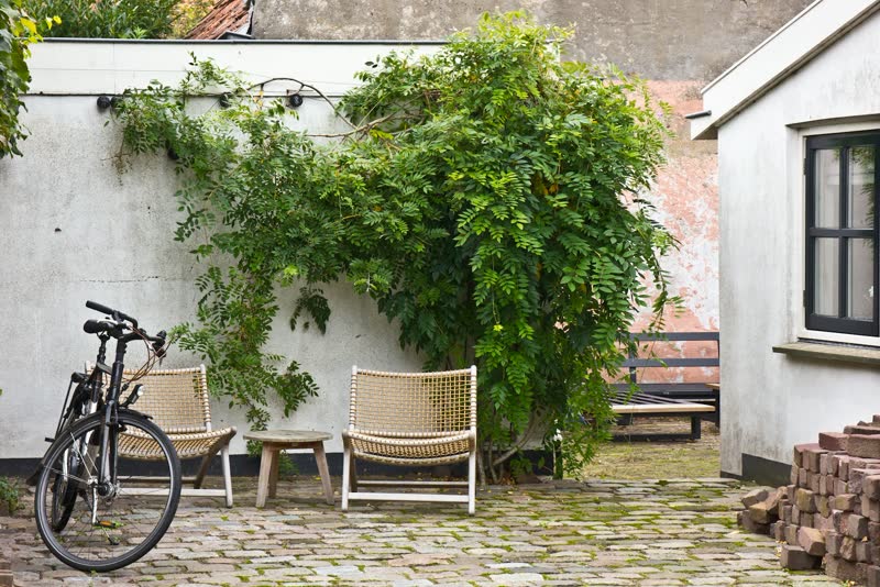 A cobbled courtyard with woven chairs and a wisteria-covered wall