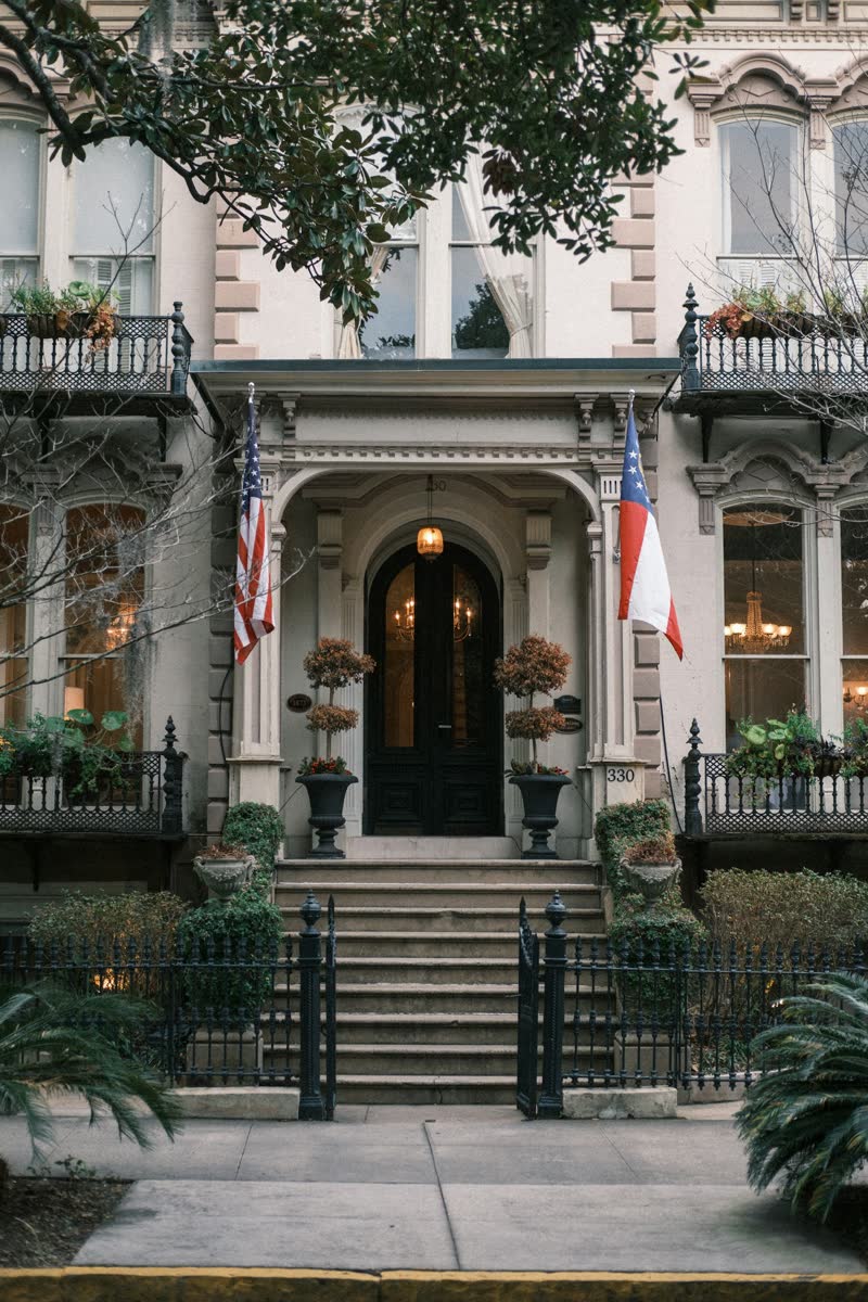 A historic townhouse entrance with flags, ironwork and a dark arched door
