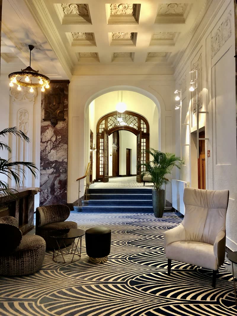 A front hall with an arched wooden door, patterned carpet and armchairs