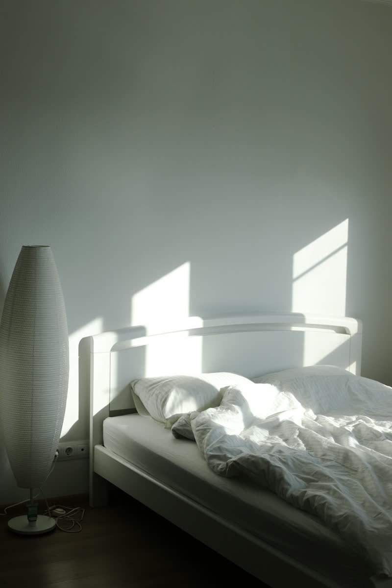 A white bed and a paper lamp in soft morning light
