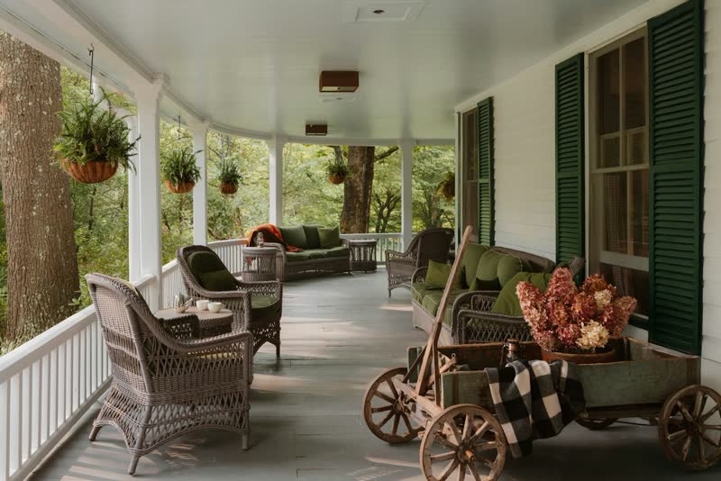 A wide wraparound porch with wicker armchairs and green shutters