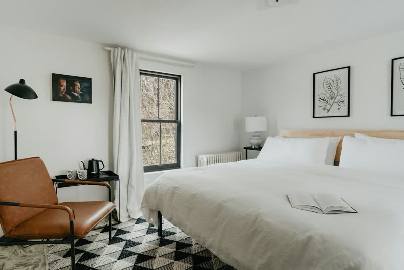A white bed under black-framed windows that look into green trees