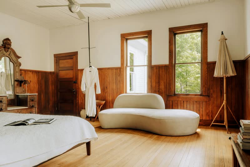 A room with heart pine floors, wood wainscot, tall windows and a curved cream sofa