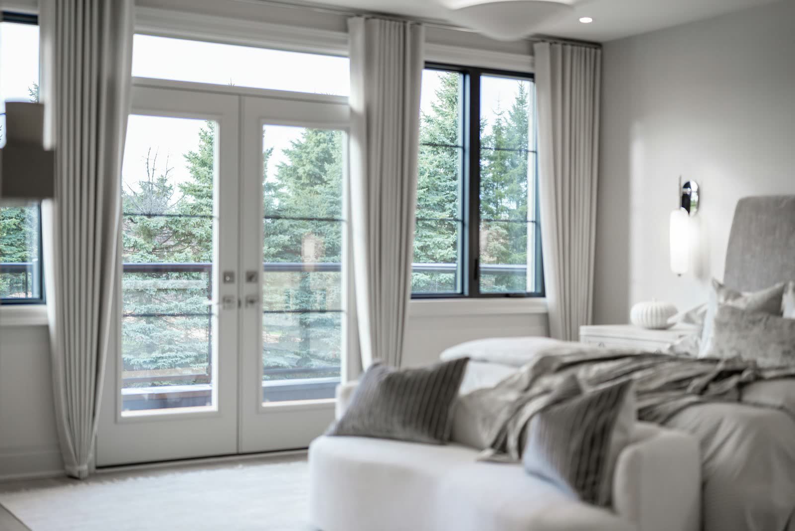 A bedroom with French doors opening to a balcony among tall trees